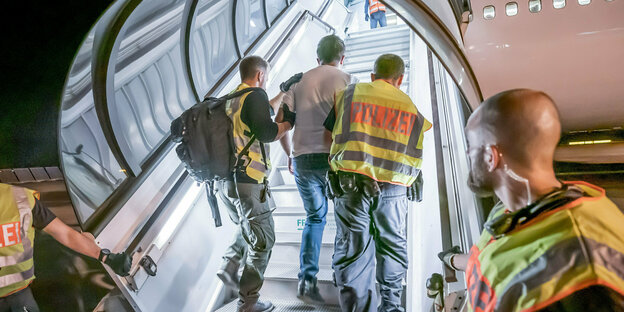 Zwei Polizisten führen einen Mann eine Gangway hinauf