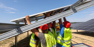 Vier Personen in gelben Warnwesten montieren ein Solarmodul auf einem Feld