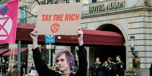 Ein Demonstran hält vorm Adlon Hotel ein Schild mit Tax the Rich hoch