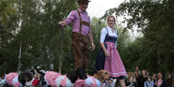 Ein Paar führt drei Dackel spazieren. Die Hunde scheinen ein Dirndl zu tragen