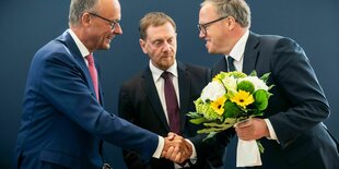 Friedrich Merz, Michael Kretschmer und Mario Voigt mit einem Blumenstraus