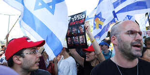 Protest mit den Flaggen israels und einem Plakat das die Porträts von sechs israelischen Geiseln der Hamas zeigt