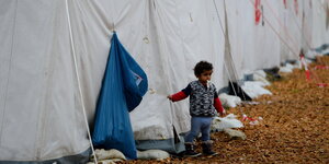 Ein Kind steht neben einem blauen Müllsack vor einer Reihe weißer Zelte