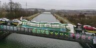 Aktivist*innen verkleiden einen VW-Autozug über dem Mittellandkanal mit einem großen Transparent. Auf dem ist eine Straßenbahn aufgemalt.