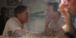 Das Standbild aus dem Film "Queer" zeigt William und Eugene einander gegenübersitzend in einer verrauchten Bar.