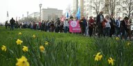 Ostermarsch in Berlin, im Vordergrund blühen die Osterglocken im Hintergrund DemonstrantInnen, inder Mitte trägt jemand ein Transparent mit einem großen Peacezeichen