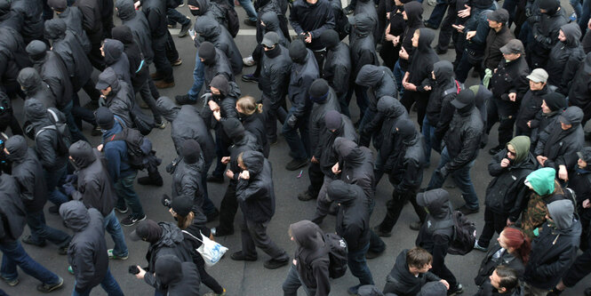 Blick von oben auf mehrere schwarz gekleidete Menschen mit Kapuze auf einer Demo