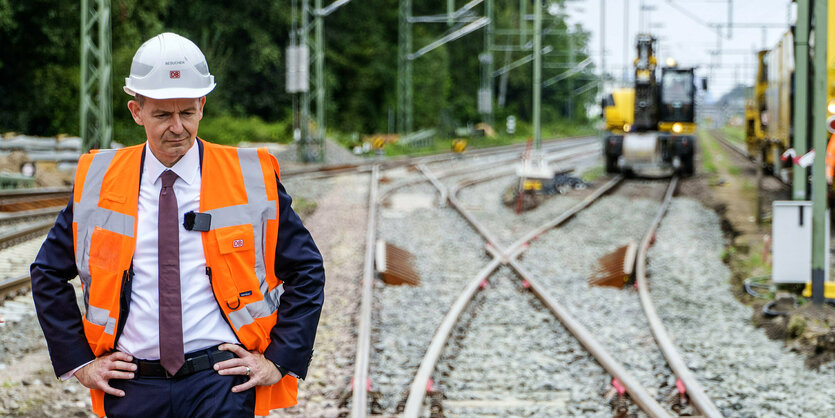 Volker Wissing mit Helm auf dem Kopf und Warnweste steht neben den Schienen an der Bauestelle der Reidbahn