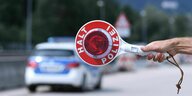 "Halt- Polizei" steht auf der roten Kelle - im Hintergrund steht ein Polizeiauto