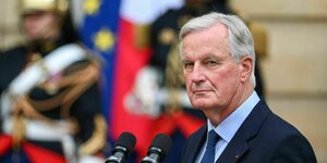 Michel Barnier steht vor dem Hotel de Matignon, hinter ihm Soldaten in bunter Uniform und er schaut zufrieden in die Kamera