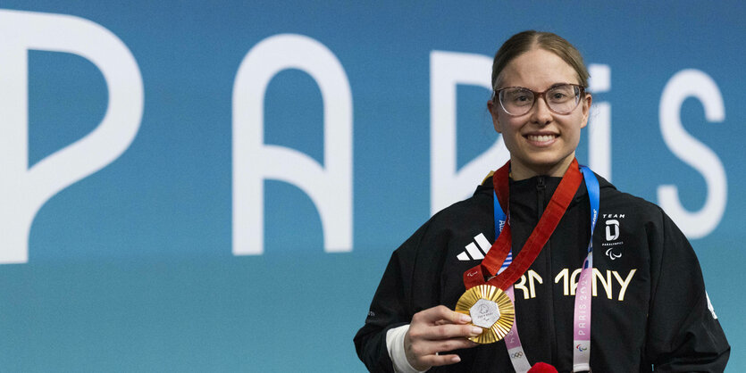 Eine junge Sportlerin zeigt stolz ihre olympische Goldmedaille.