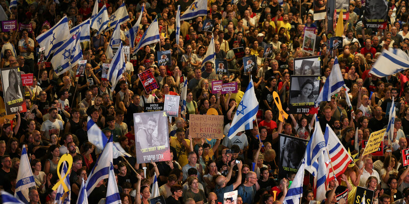 Israelfahnen und Plakate mit Bildern der Geiseln in einer nächtlichen Menschenmenge