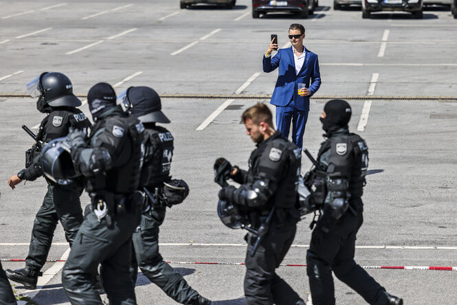 Zu sehen ist ein Abgeordneter der AfD, der auf dem Parkplatz der Grugahalle steht und mit einem Smartphone die Gegendemonstration und Polizisten filmt.