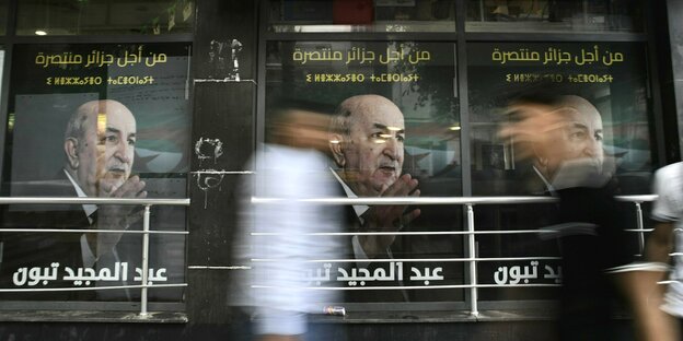 Menschen gehen an Wahlplakaten vorbei, auf denen das Porträt von Abdelmadjid Tebboune zu sehen ist