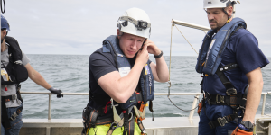 Auf einem Boot stehen drei Mechaniker mit Helm und Kletterausrüstung