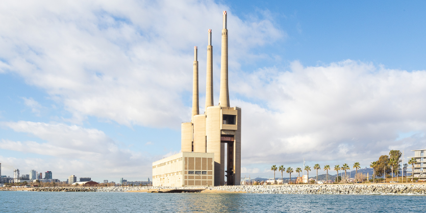 Ein Fabrikgebäude mit drei Schornsteinen neben Palmen am Meer