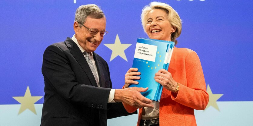 Mario Draghi übergibt Ursula von der Leyen seinen Bericht. Sie scheint überglücklich und lacht