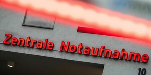 Auf einem Gebäude steht in roter Schrift: „Zentrale Notaufnahme“. Davor blinken rote Lichter.