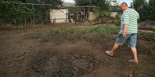 Ein Mann steht in einem Gemüsegarten und zeigt auf einen Krater im Beet