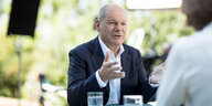 Olaf Scholz sitzt an einem Tisch in sommerlicher Stimmung und spricht