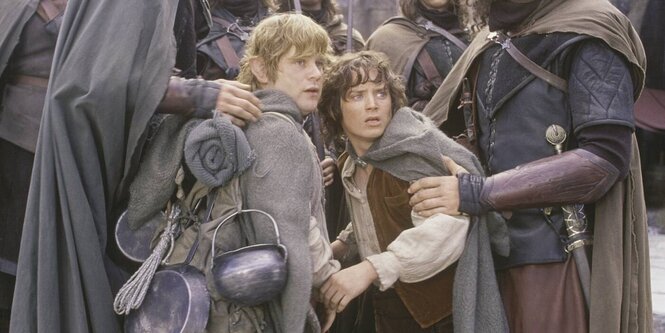 Filmstill aus "Herr der Ringe". Frodo und Sam stehen nah beisammen und schauen schockiert. An den Oberarmen werden sie von Menschen angefasst, die so groß sind, dass man ihre Köpfe ncht sieht.