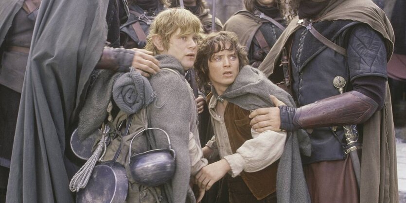 Filmstill aus "Herr der Ringe". Frodo und Sam stehen nah beisammen und schauen schockiert. An den Oberarmen werden sie von Menschen angefasst, die so groß sind, dass man ihre Köpfe ncht sieht.