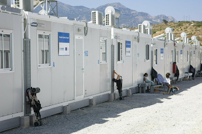 Containerartige Behausungen stehen in einer Reihe, vereinzelt spielen Kinder vor ihnen