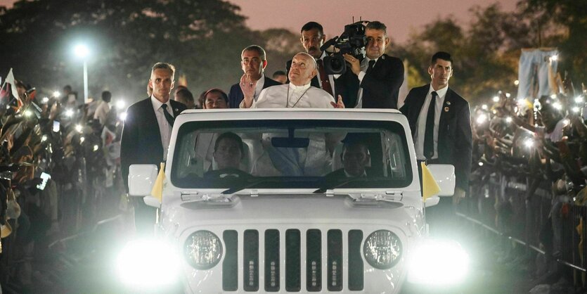 Papst Franziskus steht auf einem Auto und schaut in den Himmel, am Straßenrand bilden Menschen ein Spalier