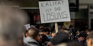 Teilnehmer einer Islamisten-Demo halten ein Plakat mit der Aufschrift „Kalifat ist die Lösung“ in die Höhe.