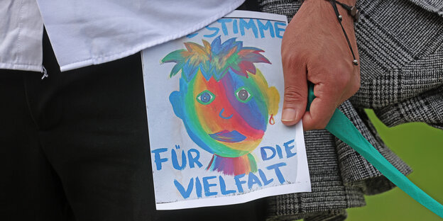 Ein Mann hält einen Flyer mit der Aufschrift "Eine Stimme für die Vielfalt" in den Händen