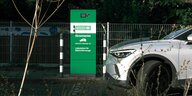 Eine Elektrotankstelle mit grüner Ladestation und hellem Auto in der Nacht