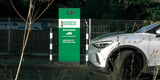 Eine Elektrotankstelle mit grüner Ladestation und hellem Auto in der Nacht