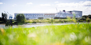 Vor einem Dock mit der Aufschrift "Jos. L. Meyer Papenburg" liegt ein Kreuzfahrtschiff im Wasser