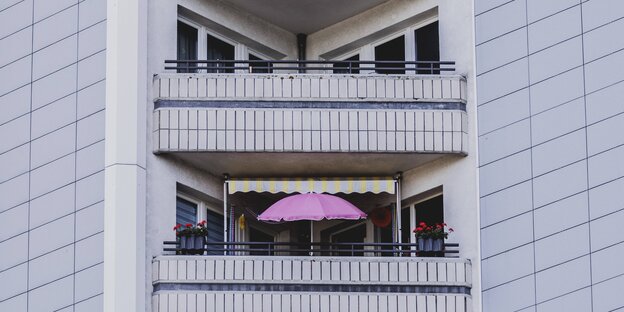 Zwei Balkone, einer mit Sonnenschirm in einem Plattenbau