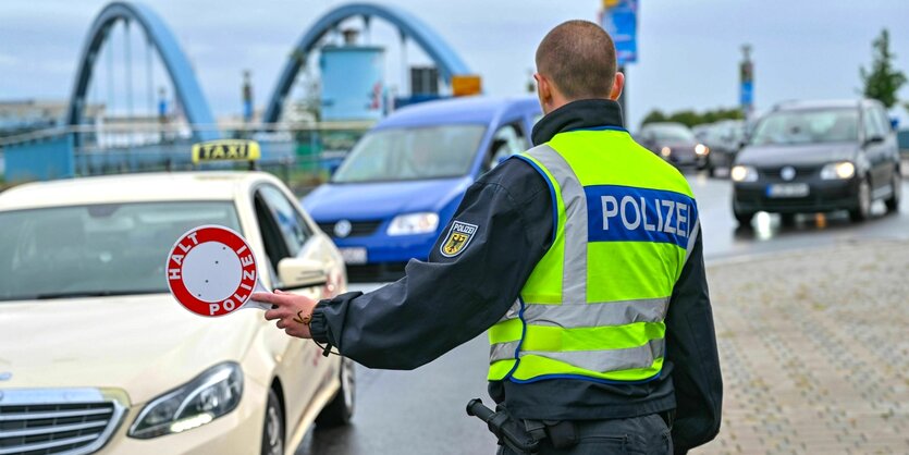 Ein Grenzpolizist mit Warnweste hält an der Grenze ein Auto an