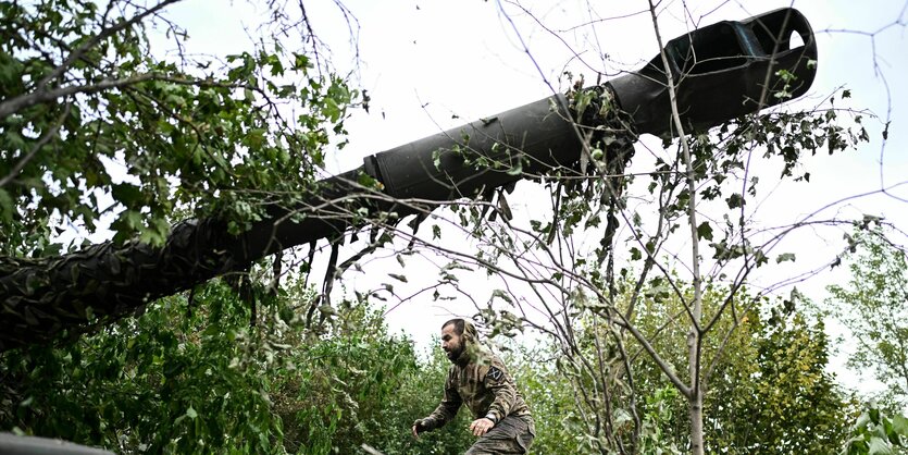 Ein russischer Soldat in Kampfuniform rennt durchs Unterholz, vor ihm das Zielrohr einer Haubitze