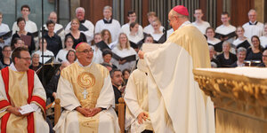 Im Osnabrücker Dom sitzt Dominicus Meier fröhlich blickend auf seinem Bischofsstuhl, während ihm Weihbischof Johannes Wübben, stehend, die Ernennungsurkunde entgegen.