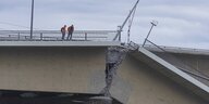 Zwei Männer in Warnwesten stehen auf einer eingestürzten brücke