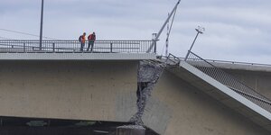 Zwei Männer in Warnwesten stehen auf einer eingestürzten Brücke