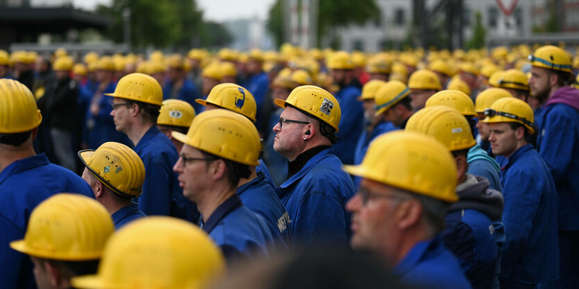 Mitarbeiter der Meyer Werft in Papenburg stehen in blauer Arbeitskleidung und gelben Helmen auf einem Hof