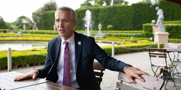 Jens Stoltenberg sitzt in einem Park mit Springbrunnen an einem Tisch