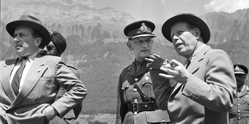 Männer in Anzügen und Uniformen vor den Bergen