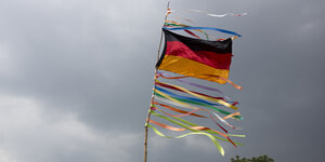 Deutschlandflagge im Wind, darunter sind bunte Flatterbänder