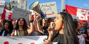 Demonstrant*innen auf der Straße, darunter viele junge Frauen. Eine von ihnen steht seitlich zur Kamera im Vordergrund und ruft etwas in ein Megaphon, dass von einer anderen Frau gehalten wird