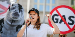 Luisa Neubauer mit Mikrofon vor Schild mit dem druchgestrichenen Wort „Gas“