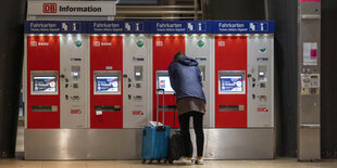 Reisende mit Rucksack und Rollkoffer vor mehreren Bahnticketautomaten