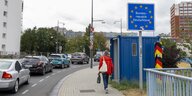 Grenzübergang in Frankfurt (Oder). Man sieht ein Grenzschild, ein schwarz-rot-gelben Grenzstein und eine Straße auf der es sich staut. In der Mitte läuft eine Person auf einem Fußgängerweg.