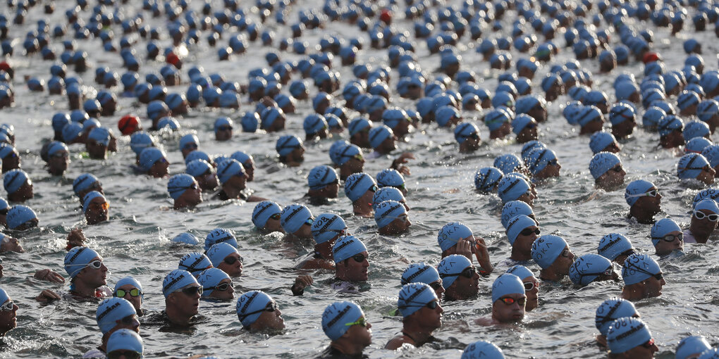 Viele Schwimmer mit Badekappe und Schwimmbrille warten im Ozean auf Startschuss