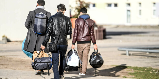 Drei Menschen tragen ihr Gepäck über einen Weg