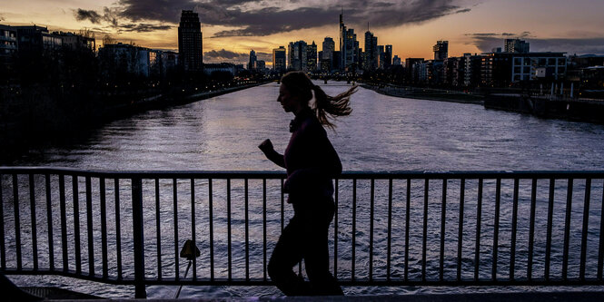 Eine Frau joggt bei Sonnenuntergang über eine Brücke in Frankfurt am Main